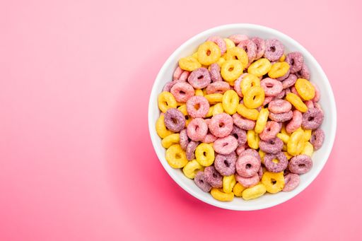 A top view of a bowl of cereal on a pink surface under the lights