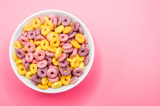 A top view of a bowl of colorful cereal on a pink surface under the lights