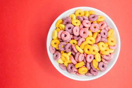 A top view of a bowl of colorful cereal on a red surface under the lights