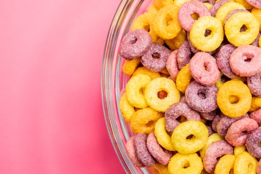 A top view of a bowl of colorful cereal on a pink surface under the lights