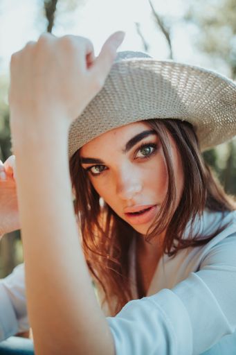 A Bosnian Caucasian woman holding a cowboy hat while looking at the camera with a serious face