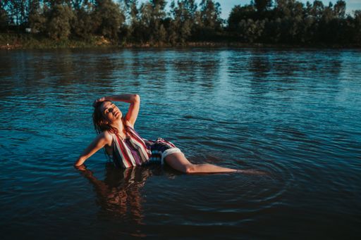 A shallow focus of a young Caucasian woman wearing a striped dress and posing in a lake in aforest
