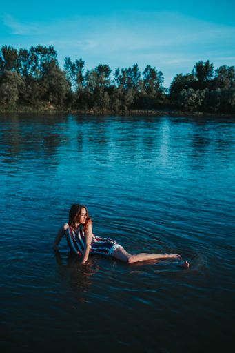 A shallow focus of a young Caucasian woman wearing a striped dress and posing in a lake in a forest