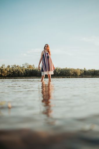 A shallow focus of a young Caucasian woman wearing a striped dress and posing in a lake in a forest