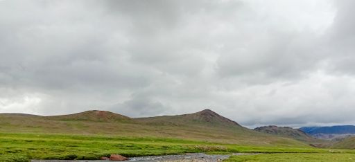 A beautiful panoramic view of a field and mountains in the background on a cloudy day