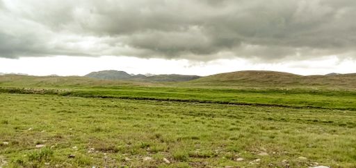 A beautiful panoramic view of a field and mountains in the background on a cloudy day