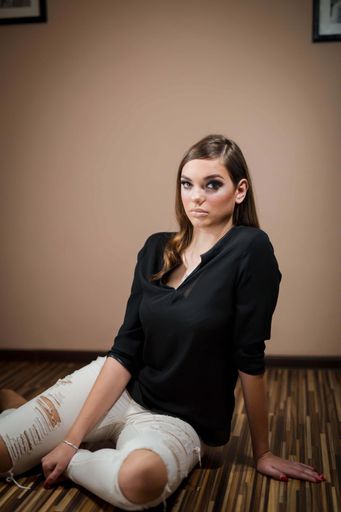 A vertical shot of a brunette female with a black shirt and white pants sitting on the floor