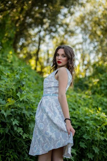 A vertical shot of a young caucasian female in a light blue summer dress posing in nature