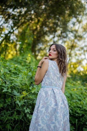 A portrait of a young sexy brunette girl in nature looking back over her shoulder in a light summer dress