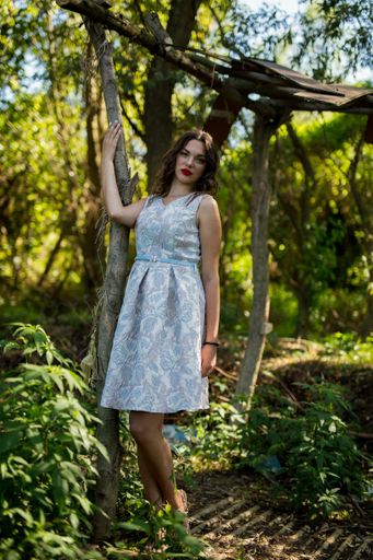 A vertical shot of a young caucasian female leaning her arm on a wooden post in a forest