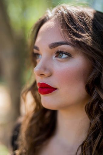 A portrait of a brunette female with red lipstick on the blurred back