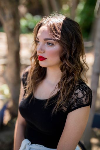 A shallow focus of a young Caucasian woman wearing a black dress with red lipstick in a forest