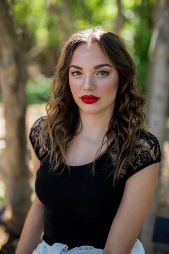 A shallow focus of a young Caucasian woman wearing a black dress with red lipstick in a forest
