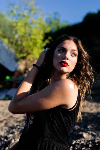 A portrait of a brunette female with red lipstick touching her hair on the blurred background