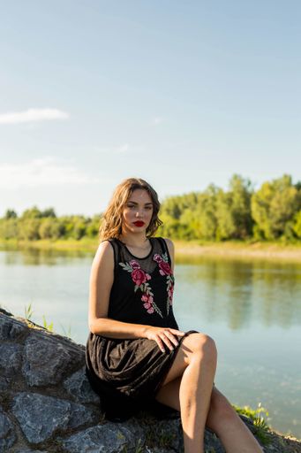 A vertical shot of a sexy Bosnian Caucasian woman sitting on a rock while posing near a river
