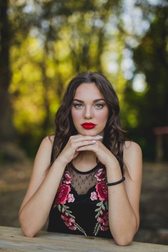 A portrait of a brunette female with red lipstick holding her hands under her chin on the blurred background