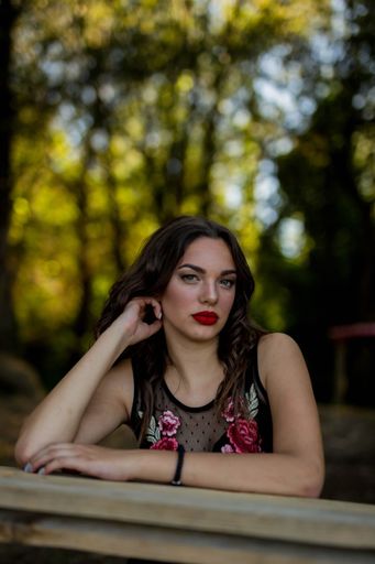 A portrait of a brunette female with red lipstick touching her hair on the blurred background