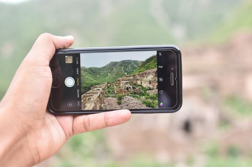 A hand holding a phone and taking a photo of the historic ruins from Bhangarh village in Alwar district, Rajasthan, India