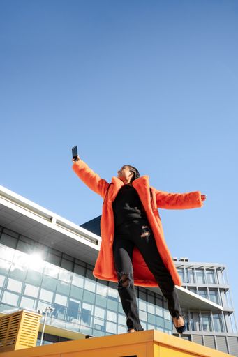 A young black female standing on a yellow surface outside and taking a selfie