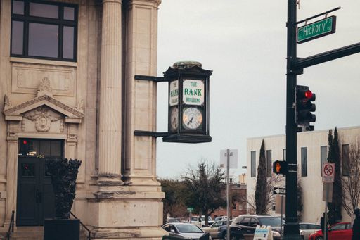 A clock attached to a building near the road with cars