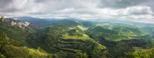 A panoramic aerial view of green mountains with a cloudy sky in the background