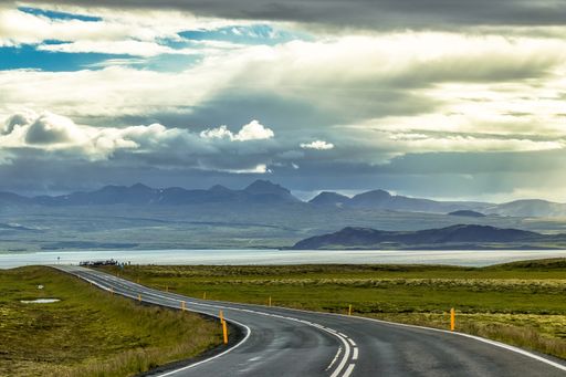 A closeup shot of a curvy road surrounded by hills and fields under a cloudy sky in Iceland