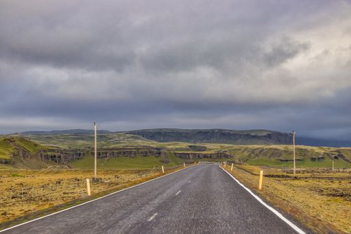 A closeup shot of an empty road surrounded by hills and fields under a cloudy sky in Iceland