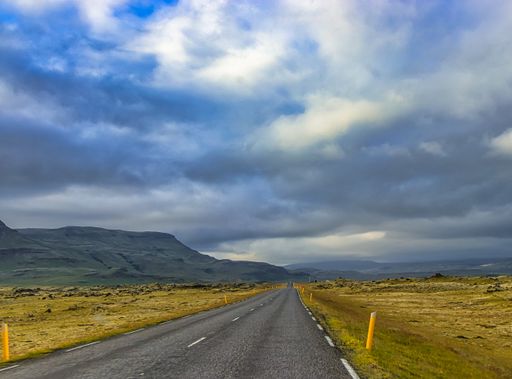 A closeup shot of an empty road surrounded by hills and fields under a cloudy sky in Icelan
