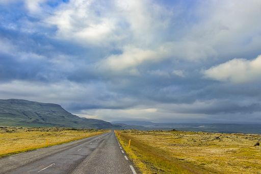 A closeup shot of an empty road surrounded by hills and fields under a cloudy sky in Iceland