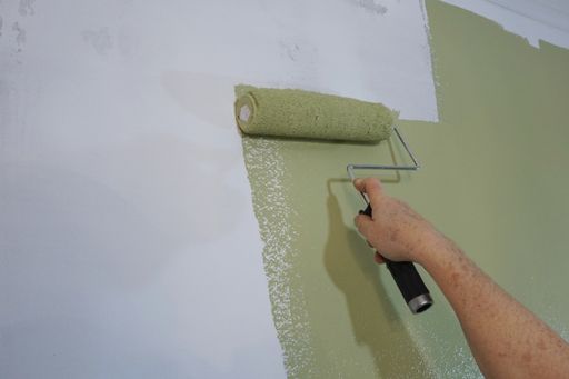 Close-up of a hand and a paint roller applying green paint to a wall in a remodeling project.