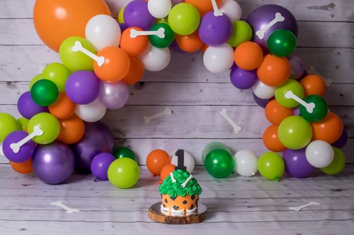 A small creamy birthday cake with decorative bones and colorful balloons on the background