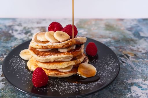 A close-up image of a stack of fluffy pancakes with fruit and maple syrup