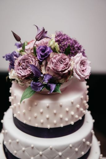 A vertical shot of a delicious wedding cake decorated with purple flowers.