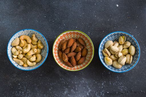 A top view of almonds, cashews and coasted nuts in bowls on the table