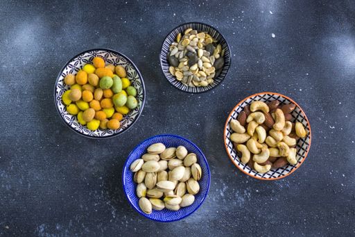 A top view of almonds, cashews and coasted nuts in bowls on the table