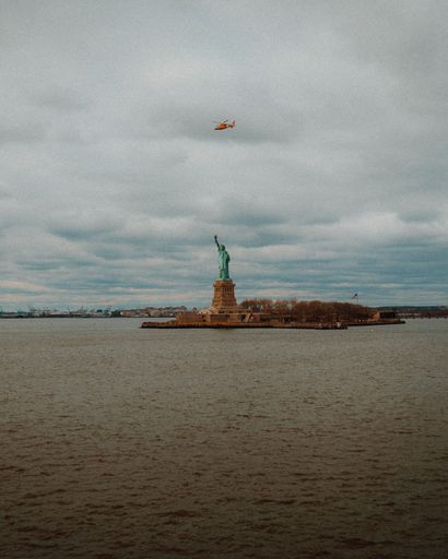 Aerial view of a helicopter flying over the iconic Statue of Liberty in New York City skyline on a cloudy day