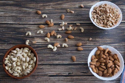A variety of assorted nuts are presented in bowls on a wooden table