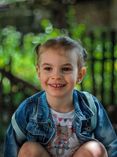 A vertical closeup shot of a little girl in a cute denim jacket laughing and having fun in a park