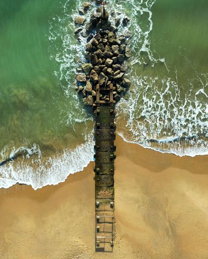An aerial shot of a wooden pier on the beach on a sunny day