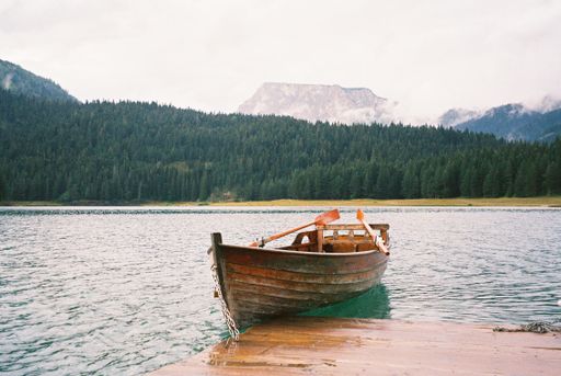 An old wooden boat in a lake with mountains and spruce forest in the background