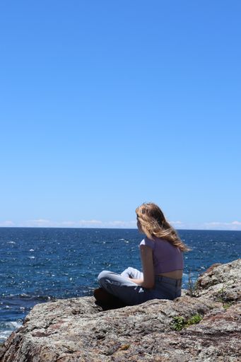 Blonde Hair young girl reading in the rocks with sea view in a summer day with clear blue sky