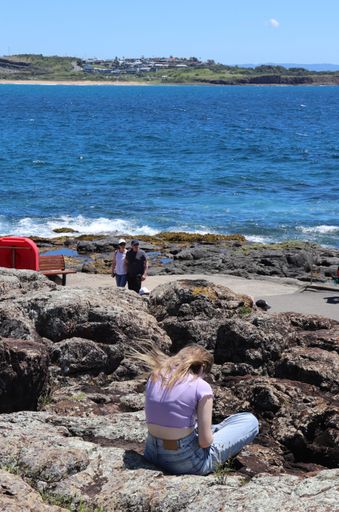 Blonde Hair young girl reading in the rocks with sea view in a summer day with clear blue sky