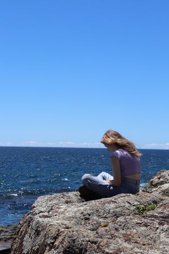 Blonde Hair young girl reading in the rocks with sea view in a summer day with clear blue sky