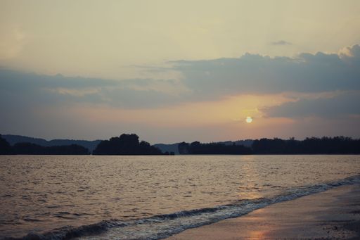 A tranquil ocean reflecting the warm orange and pink hues of the setting sun, with a few fluffy clouds in the sky