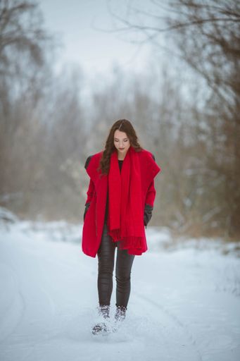 A vertical shot of a stylish brunette female in a red coat walking on a snow
