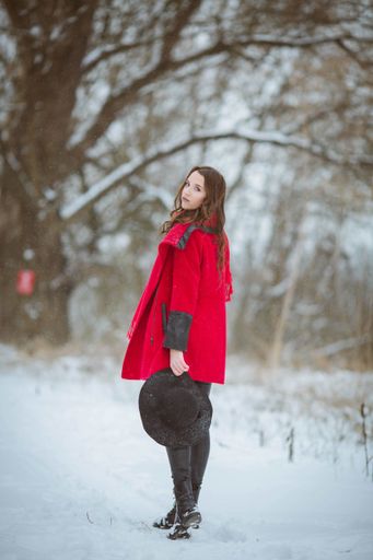 A vertical shot of a stylish female in a red coat walking on a snowy trail