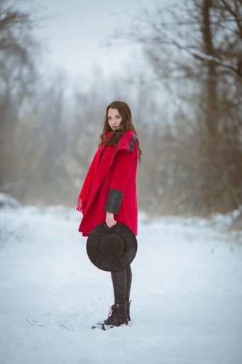 A selective focus shot of a beautiful Caucasian woman wearing a red coat in a winter forest