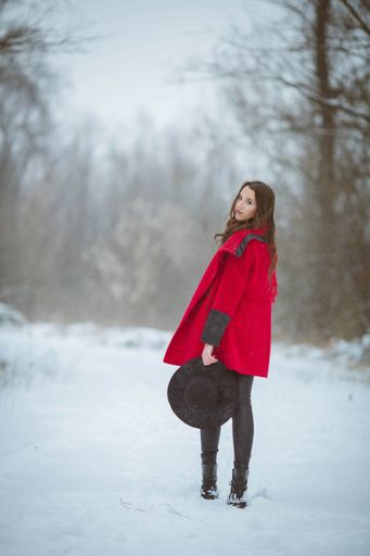 A full body shot of a young brunette girl wearing a stylish red coat in a snowy forest