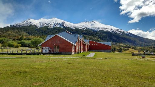 A view of a red ranch building in the middle of the field with snowy hills in the background on a sunny day
