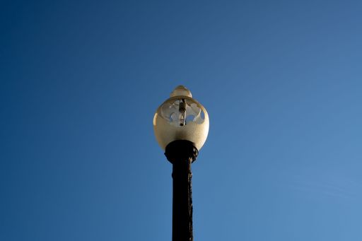 A low angle shot of a metal pole with a broken light under a blue sky